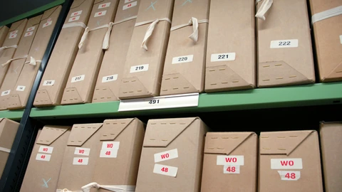 Rows of brown archival boxes on metal repository shelving, with paper labels facing the aisle.