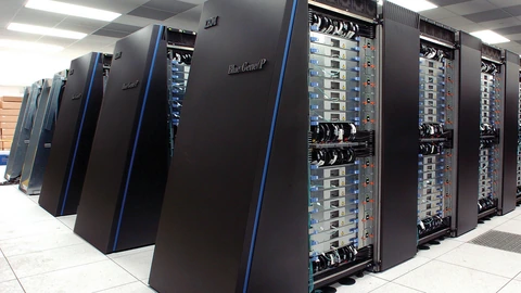Black IBM Blue Gene/P cabinets in a white machine room, nearest door labeled BlueGene/P, cable loops visible on open racks. No people appear.