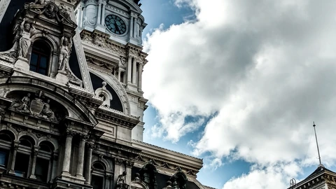 Philadelphia City Hall tower and sculpture-covered west facade against a cloudy sky, with a clock face on the tower. No living people appear.