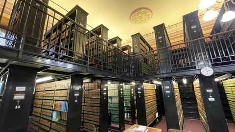 Two storeys of black metal law-book stacks with a mezzanine railing and a round wall clock.