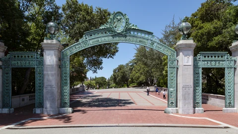 The green metal arch of Sather Gate at UC Berkeley spanning a brick plaza under a clear sky, with SATHER GATE lettering on the span.