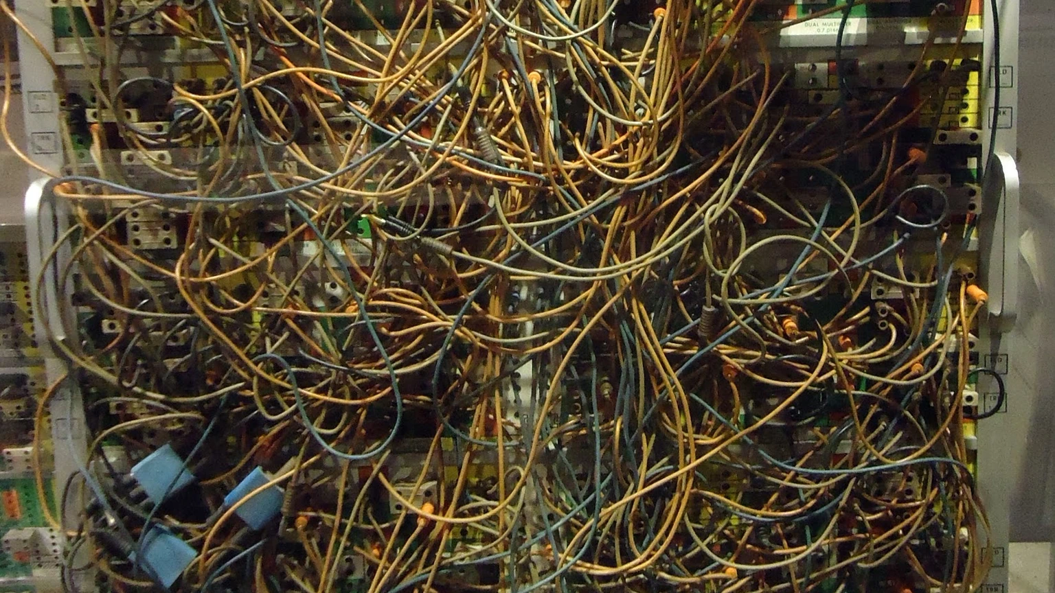 Close-up of a dense analog-computer plugboard with overlapping tan and blue patch cords on a white panel. No people appear.