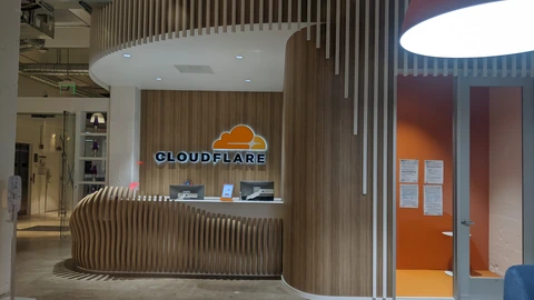 Empty Cloudflare reception desk with a wood-slat counter, cloud logo, and CLOUDFLARE lettering on a wood wall. No people appear.