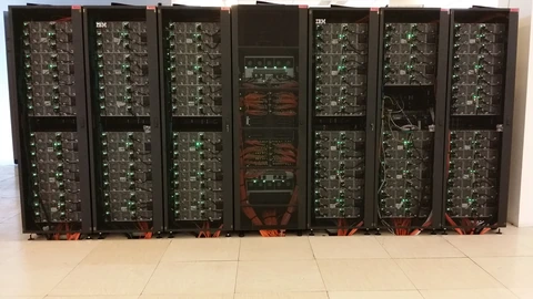 Six black IBM server racks of the Galileo supercomputer standing on a pale tiled floor, with green status LEDs and orange cables at the base.
