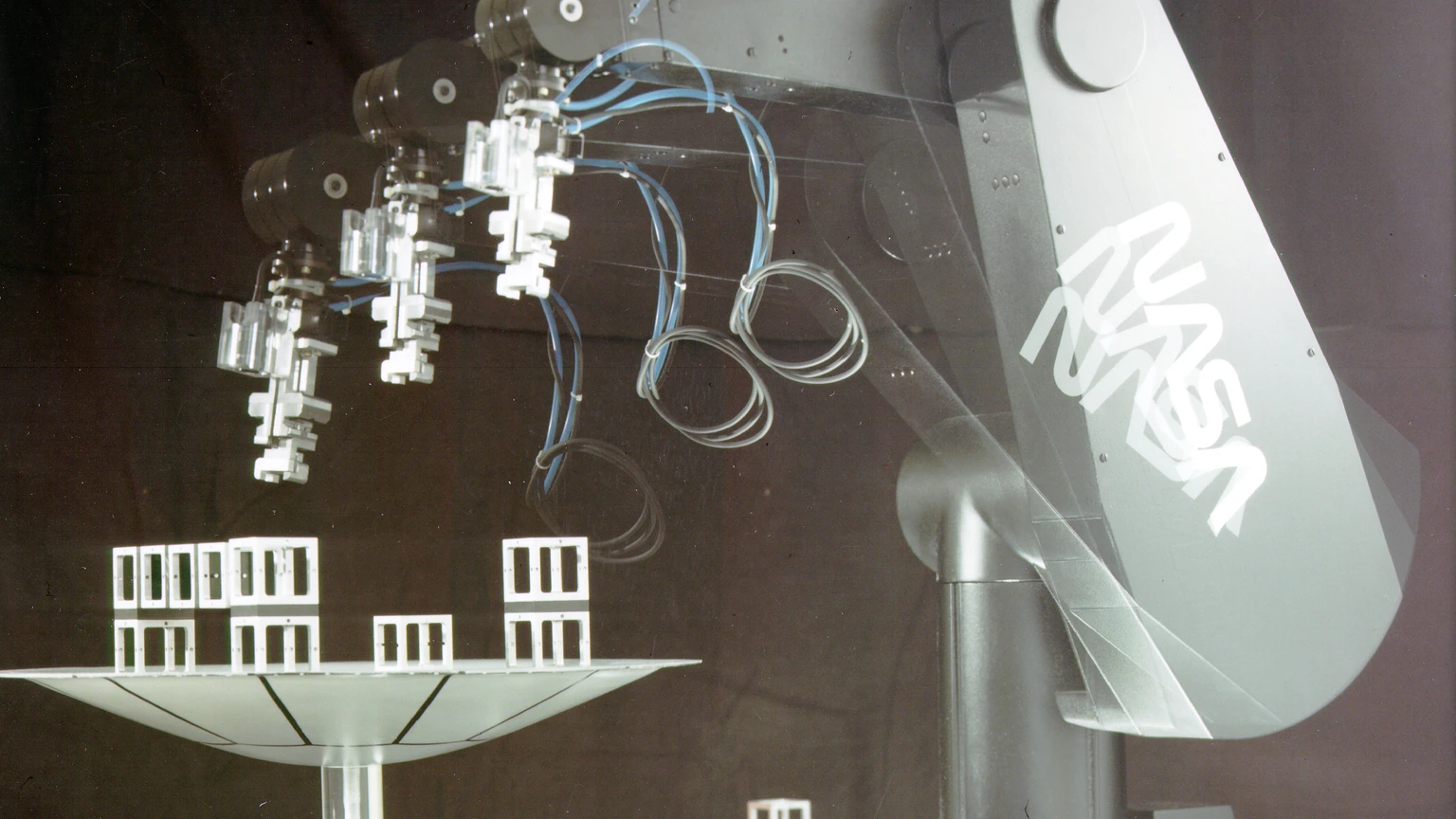 A black PUMA robotic arm with NASA lettering on a black background, hovering over a white dish of block shapes. No people appear.