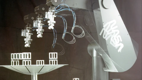A black PUMA robotic arm with NASA lettering on a black background, hovering over a white dish of block shapes. No people appear.