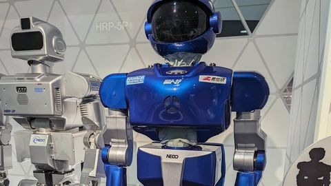 A blue Kawada HRP-2P humanoid robot standing next to a silver HRP-3P unit in a museum display, with an HRP-5P wall label behind them.
