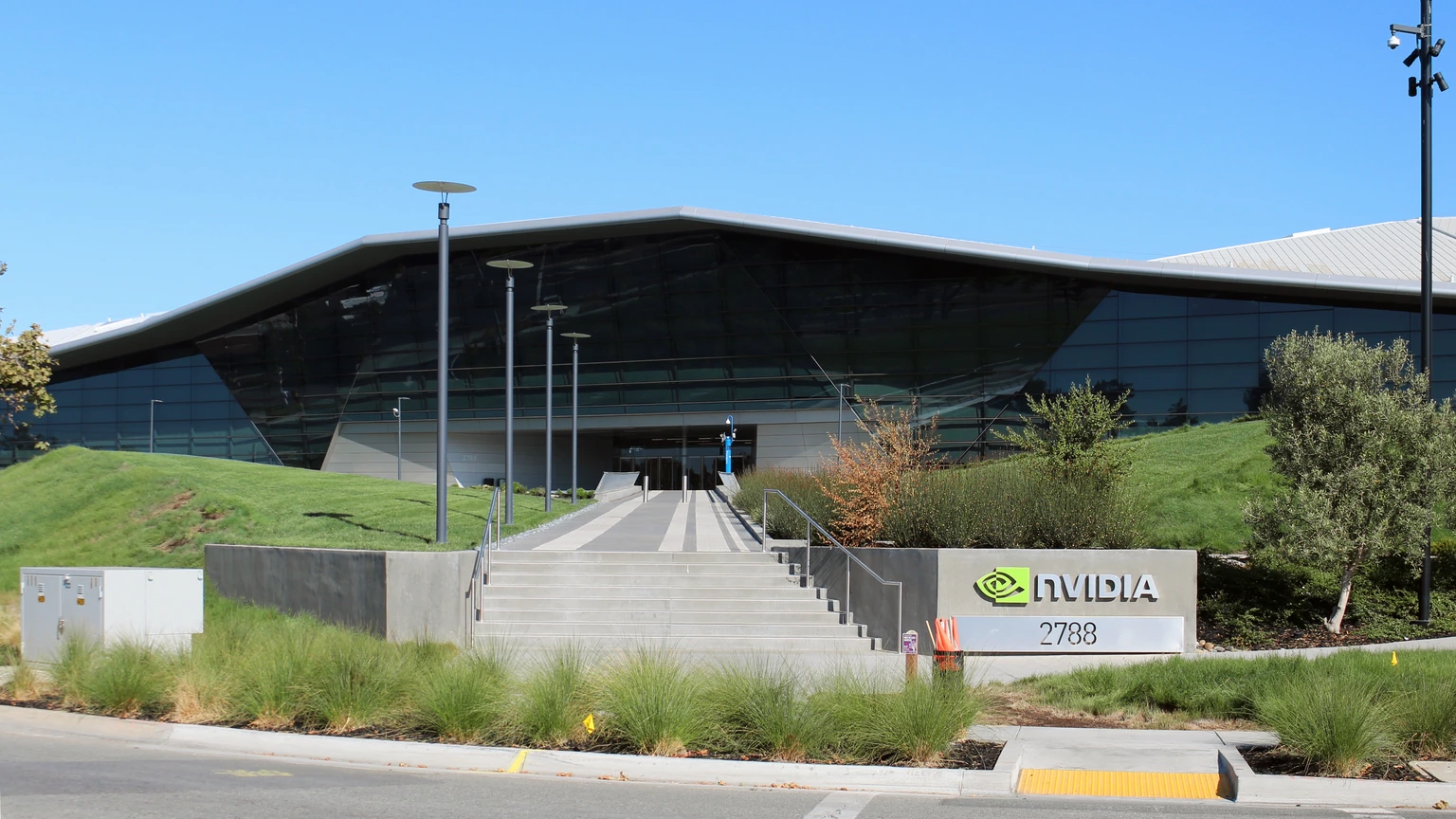 A glass NVIDIA headquarters entrance with a triangular roof, a flight of steps, and a sign reading nvidia 27888.