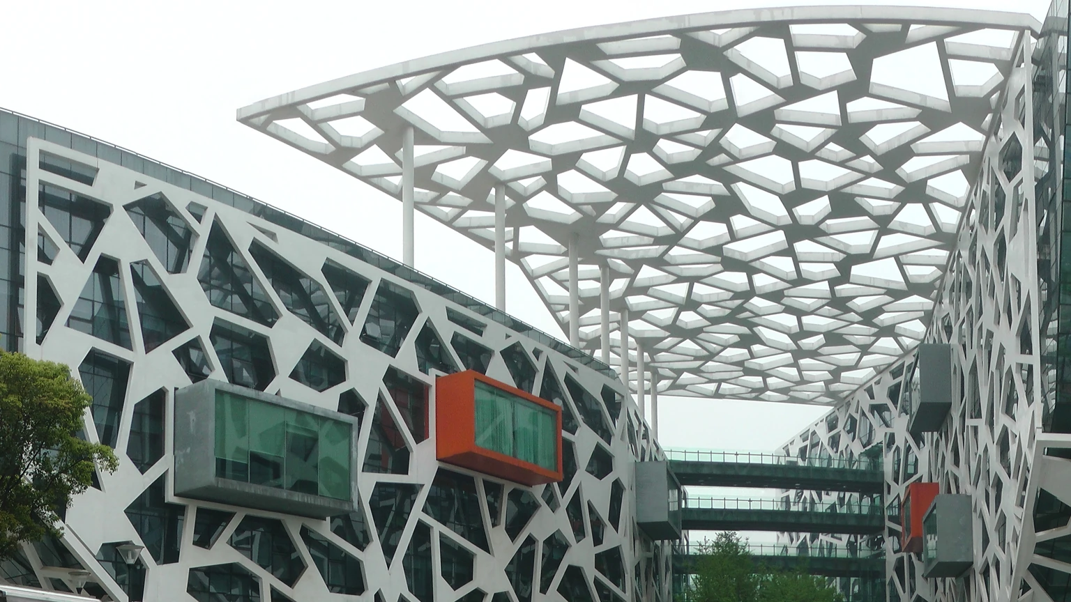 White lattice facade and geometric canopy of Alibaba’s Hangzhou headquarters, with orange-trimmed projecting rooms. No people appear.