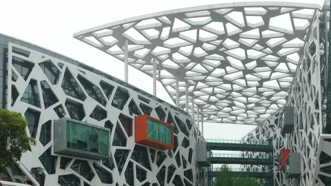 White lattice facade and geometric canopy of Alibaba’s Hangzhou headquarters, with orange-trimmed projecting rooms. No people appear.