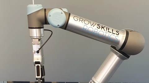A silver-and-grey Universal Robots UR5 arm marked GROW SKILLS ROBOTICS, gripper down, against a plain grey wall. No people appear.