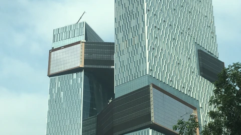 Two glass office towers joined by dark skybridges, Tencent Binhai Mansion in Shenzhen, with a tree at the right edge. No people appear.