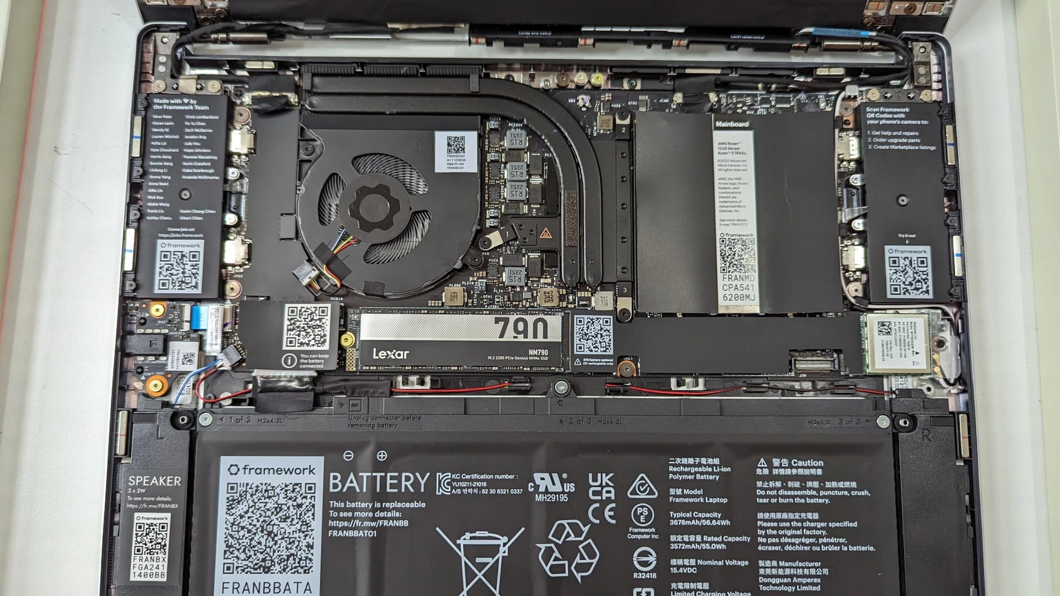 Open Framework Laptop 13 chassis showing the motherboard, fan heat pipe, Lexar 7900 NVMe drive, wireless module and Framework battery. No people appear.
