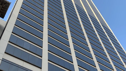 Looking up the dark glass facade of Spear Tower against a clear sky, with a pale vertical mullion and a sliver of a neighboring roof at left. No people appear.