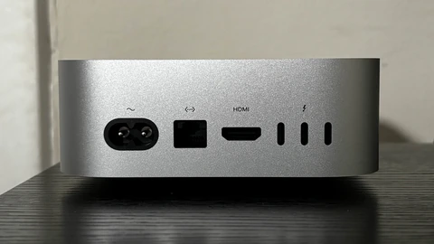 The rear ports of a silver Mac mini on a wooden surface. No people appear.