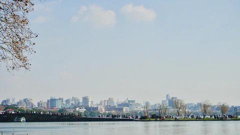 Hangzhou skyline of glass towers across West Lake under a clear sky. No identifiable people appear.