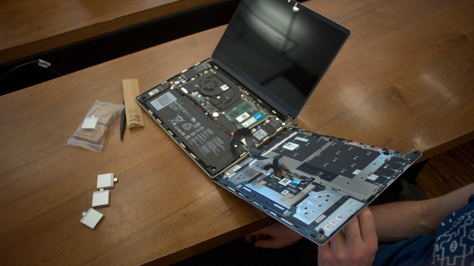 An open Framework Laptop on a wooden desk showing a dark desktop, with a second laptop behind it. No people appear.