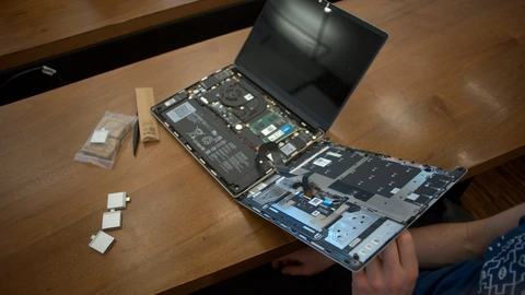 An open Framework Laptop on a wooden desk showing a dark desktop, with a second laptop behind it. No people appear.