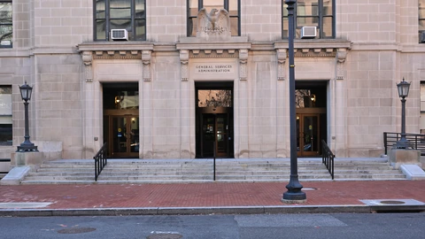 GSA headquarters entrance on F Street in Washington, D.C., with banners and an empty sidewalk. No identifiable people appear.