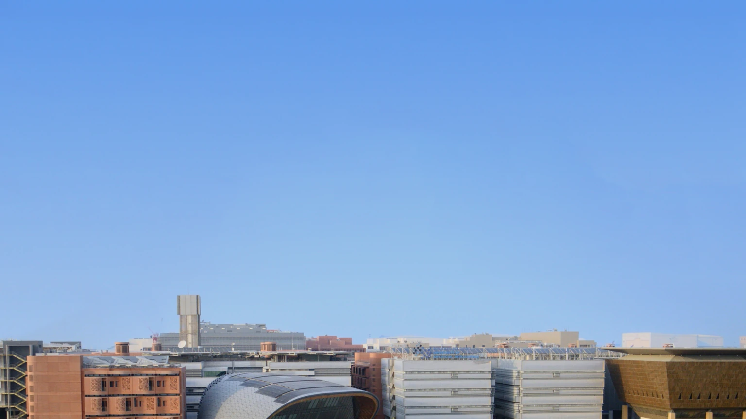 MBZUAI Knowledge Center and surrounding Masdar City campus buildings around a circular lawn and palm trees under a clear sky. Distant pedestrians may appear tiny on walkways; none are identifiable subjects of this story.