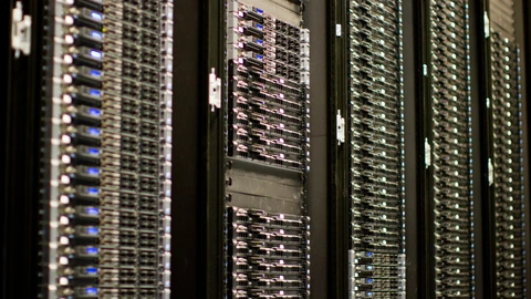 Rows of illuminated server cabinets in a data-center aisle with blue and white status LEDs. No people appear.