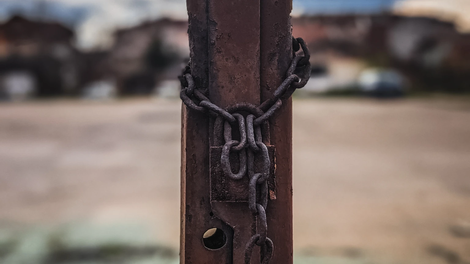 Close-up of a rusty padlock and chain on a metal fence, high contrast. No people appear.