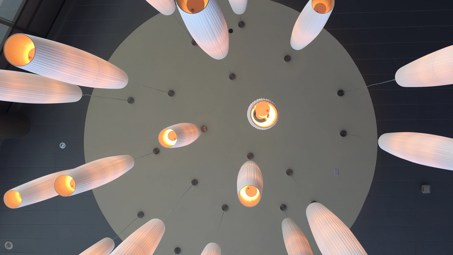 Looking up at hanging lamps in an empty glass atrium. No people appear.
