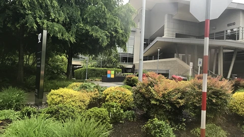 Microsoft logo sign and Building 92 visitor-center entrance on the Redmond campus with landscaping in the foreground. No people appear.