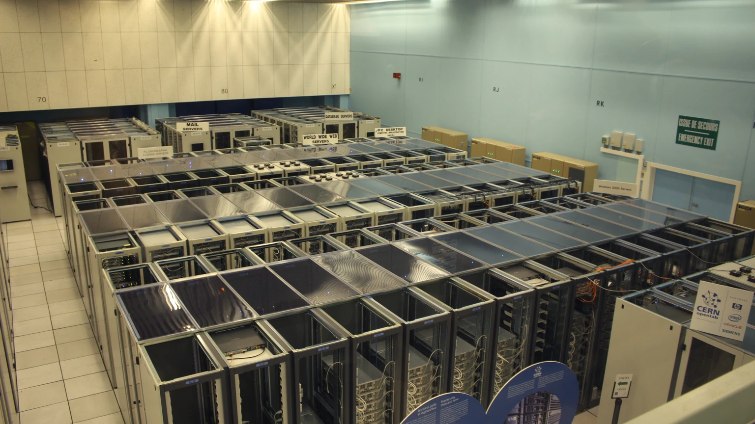 Elevated view of CERN server-room aisles with rows of racks and a World Wide Web Servers sign. No people appear.