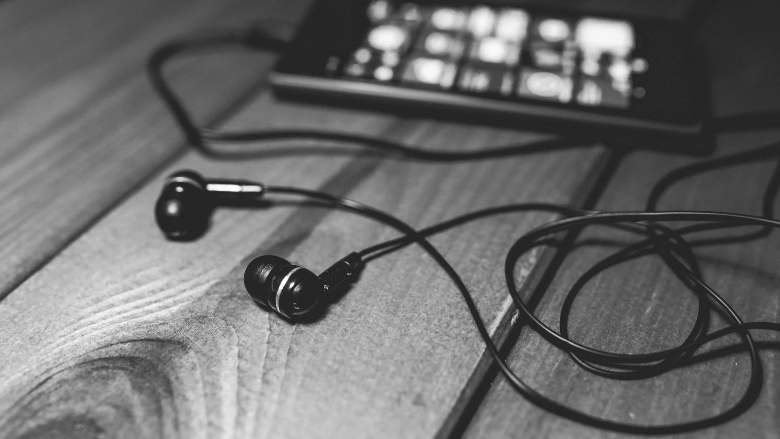 Over-ear headphones resting on a wooden desk beside a tablet and small speakers. No people appear.