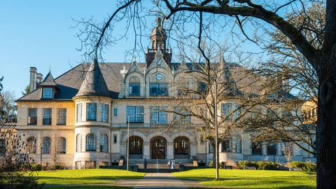 Denny Hall on the University of Washington Seattle campus, a stone collegiate building with a clock tower and south facade under a clear sky. No people appear.