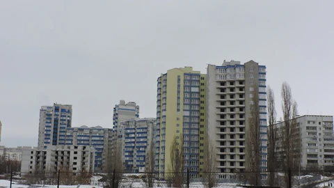 Winter view of high-rise apartment buildings on Dzherelna Street in Kharkiv, behind a snowy field and a chain-link fence.