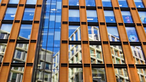 Close-up of the facade of 6 Pancras Square in London: vertical orange terracotta-coloured fins between blue glass windows that reflect nearby buildings.