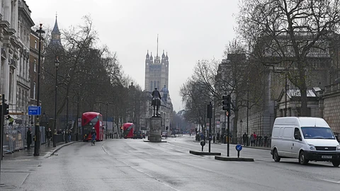 A wide, quiet Whitehall street on an overcast day, with bare trees, a mounted statue in the middle of the road, red double-decker buses and the Victoria Tower of Parliament in the distance.