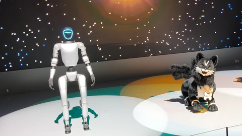 A white Unitree G1 humanoid robot with a glowing ring around its head stands on a lit stage under a starry video wall, beside a furry black-and-white robot fox.