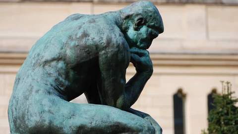 Close-up of Rodin’s bronze sculpture The Thinker, a seated figure with its chin resting on one hand, its green patina set against the pale stone wall of the Musée Rodin.