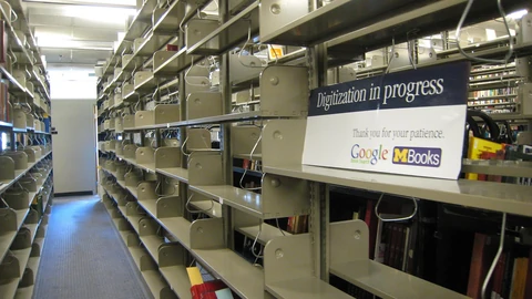 Rows of empty metal library shelves stretching into a large reading room with tall windows.