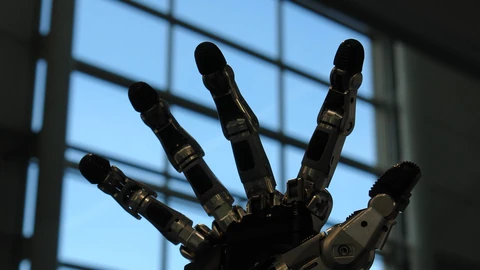 Silhouette of an anthropomorphic five-finger robot hand with metal finger joints, raised in front of a tall window.