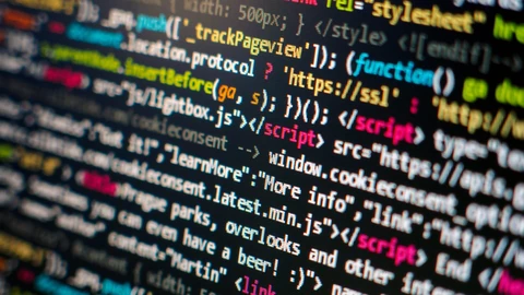 Close-up of syntax-highlighted HTML and JavaScript on a dark computer screen, with keywords and strings in green, red, yellow and blue, angled so the text recedes out of focus.