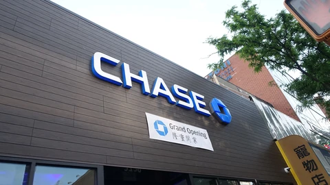A large white-and-blue CHASE sign with the bank’s blue octagon logo on the dark wood-panelled front of a new branch, with a Grand Opening banner below it.