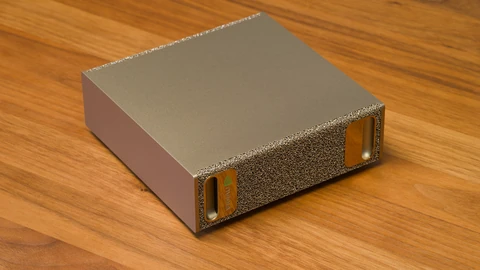 An NVIDIA DGX Spark, a small square gold-coloured desktop computer with a textured metal-foam front and a green NVIDIA logo, sitting on a wooden desk.