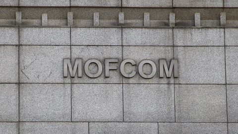 Raised metal letters spelling MOFCOM mounted on a grey granite wall of China's Ministry of Commerce building.