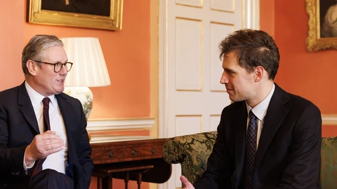 Mistral AI chief executive Arthur Mensch, in a dark suit and tie, sits on a green sofa and listens as UK Prime Minister Keir Starmer speaks to him in a room at 10 Downing Street.