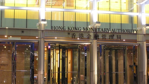 The illuminated entrance of the Hong Kong Monetary Authority at night, with HONG KONG MONETARY AUTHORITY and its Chinese name in large letters above revolving glass doors.