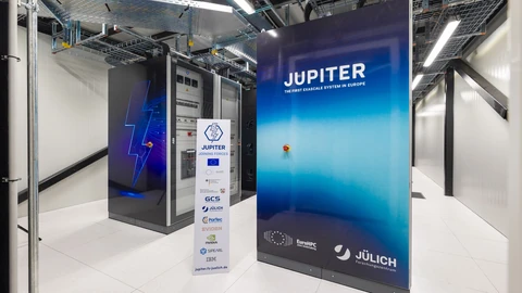 Racks of the JUPITER supercomputer in a white machine hall at Jülich, with a tall blue panel reading JUPITER, the first exascale system in Europe, a cabinet marked with a lightning bolt and a sponsor banner listing EuroHPC, Jülich, ParTec, Eviden and NVIDIA.