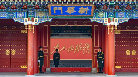 Xinhuamen, the red and gold gate of the Zhongnanhai government compound in Beijing, with three honour guards standing beneath its painted eaves and blue name board.
