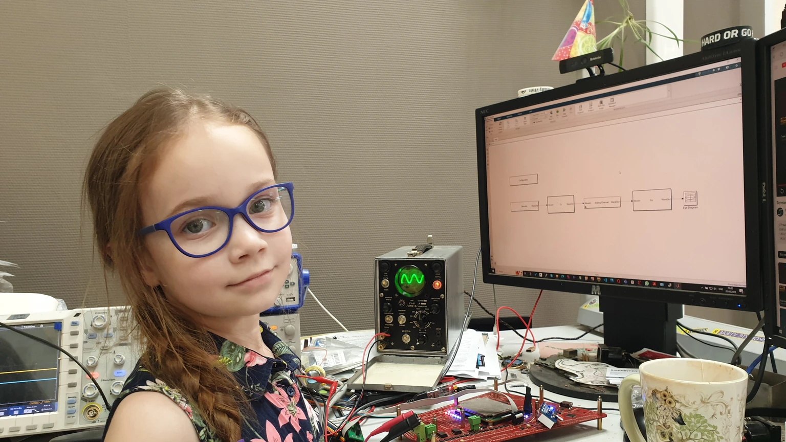 A scientist seated at a computer beside laboratory electronics.