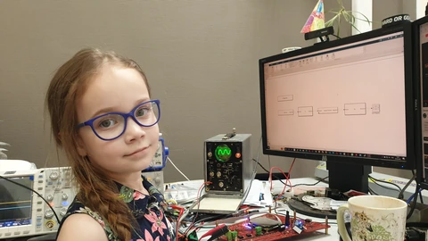 A scientist seated at a computer beside laboratory electronics.