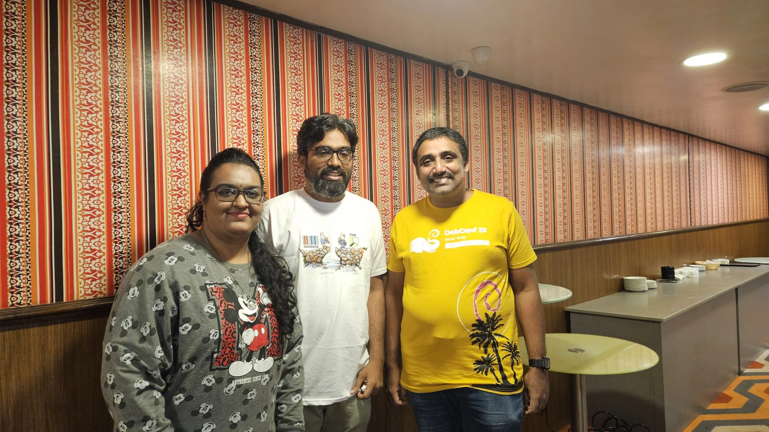 Three Indic Wikimedia Hackathon participants standing beside laptops.