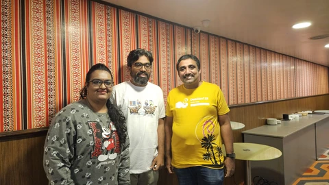 Three Indic Wikimedia Hackathon participants standing beside laptops.